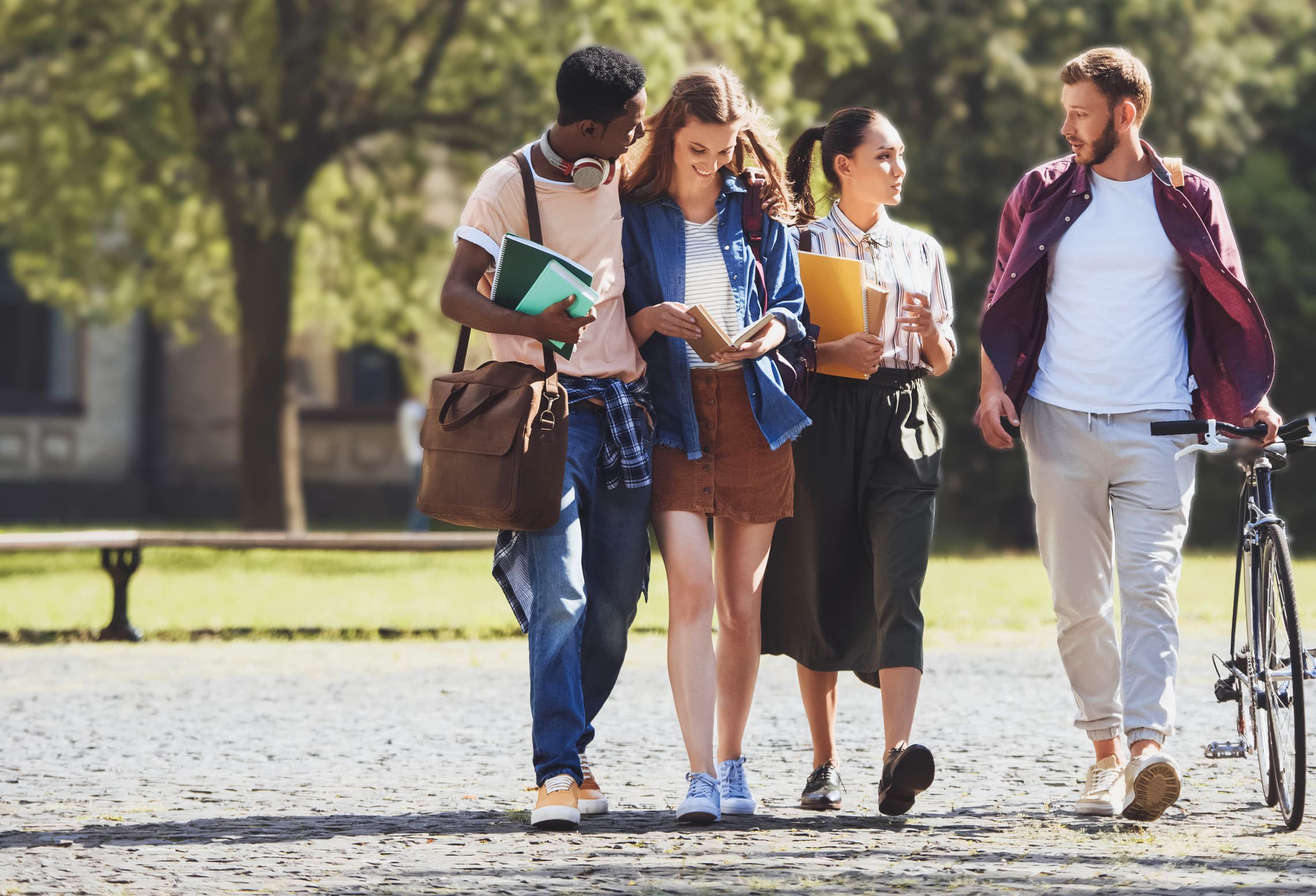 Four people walk side by side and one pushes a bicycle