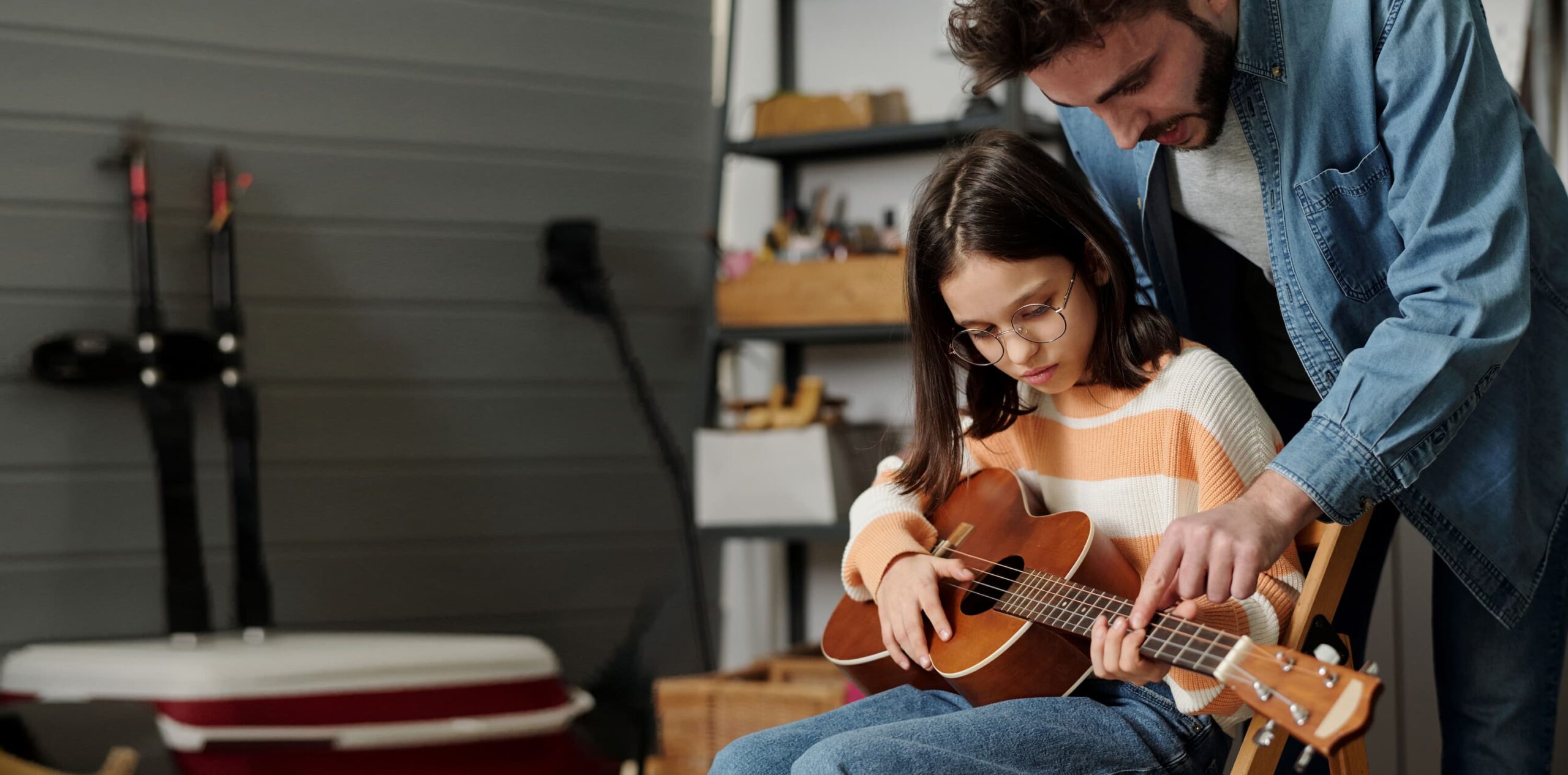 Ein Mann zeigt einem Kind, das eine Gitarre hält, wie man Gitarre spielt